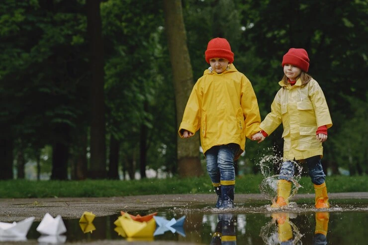 morsomme barn i regnstøvler som leker med papirskip 